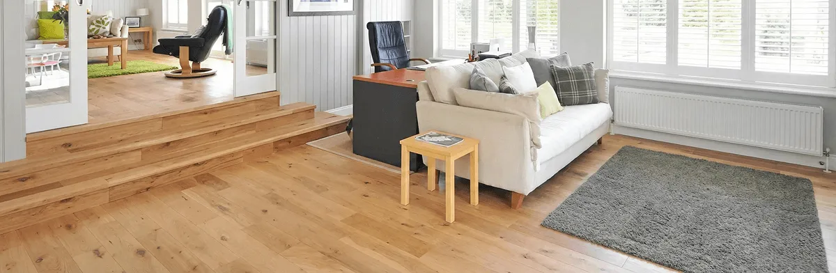 A modern living room with professionally installed laminate flooring, a beige sofa, a small side table, a gray rug, and large windows with white shutters in Peoria, IL